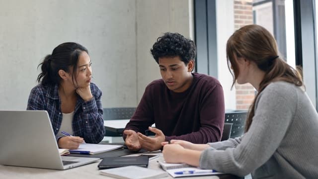 Students discuss a missed lab project deadline in a campus study room.