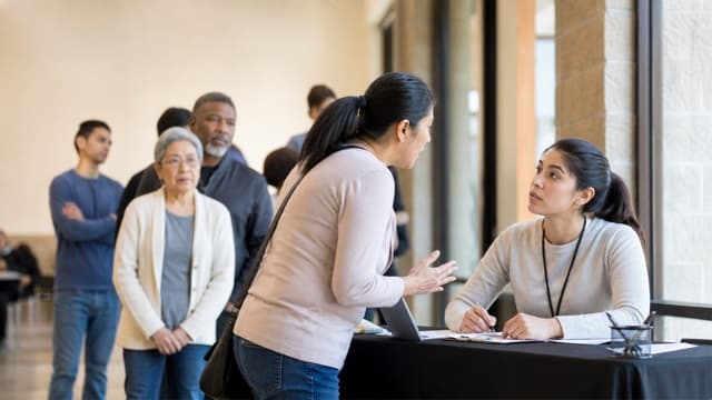 A volunteer speaks with a late arrival near a health screening line.
