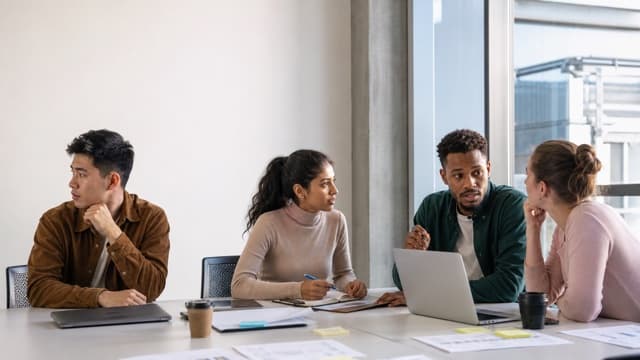 A project team meets while one member sits apart from the conversation.